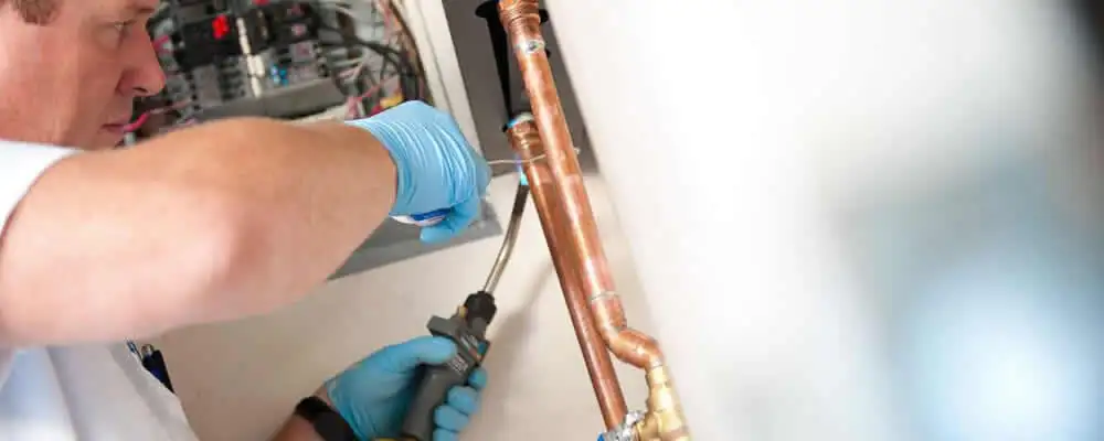 Water heater repair technician testing copper pipe connections and controls in Atlanta, GA